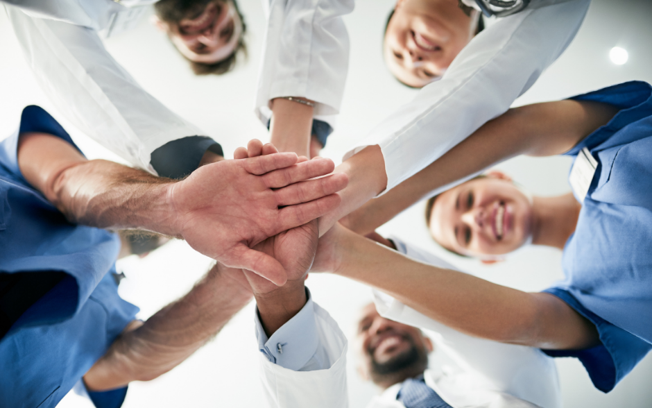 A photograph taken from below showing a group of clinicians in a circle, placing their hands on top of one another's.